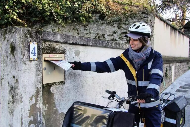 Une postière glisse une enveloppe dans une boite aux lettres. Photo La Poste