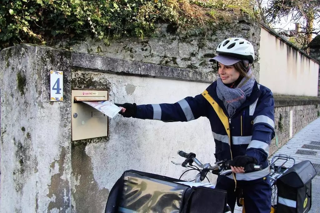 Une postière glisse une enveloppe dans une boite aux lettres. Photo La Poste